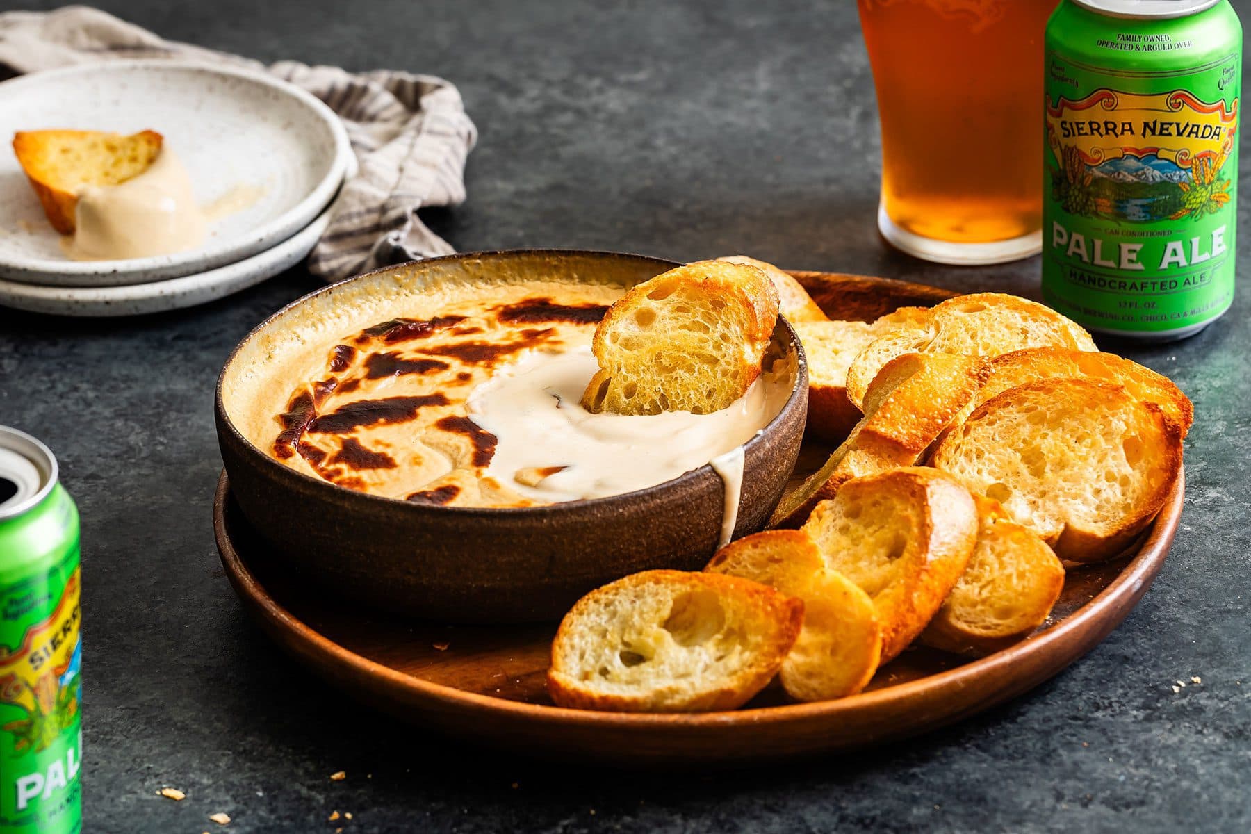 A plate of crostini bread and beer cheese dip next to a can and glass of Sierra Nevada Pale Ale